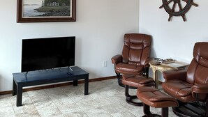 A living room with a TV, leather chairs, a wooden ceiling, and a ship's wheel decoration.