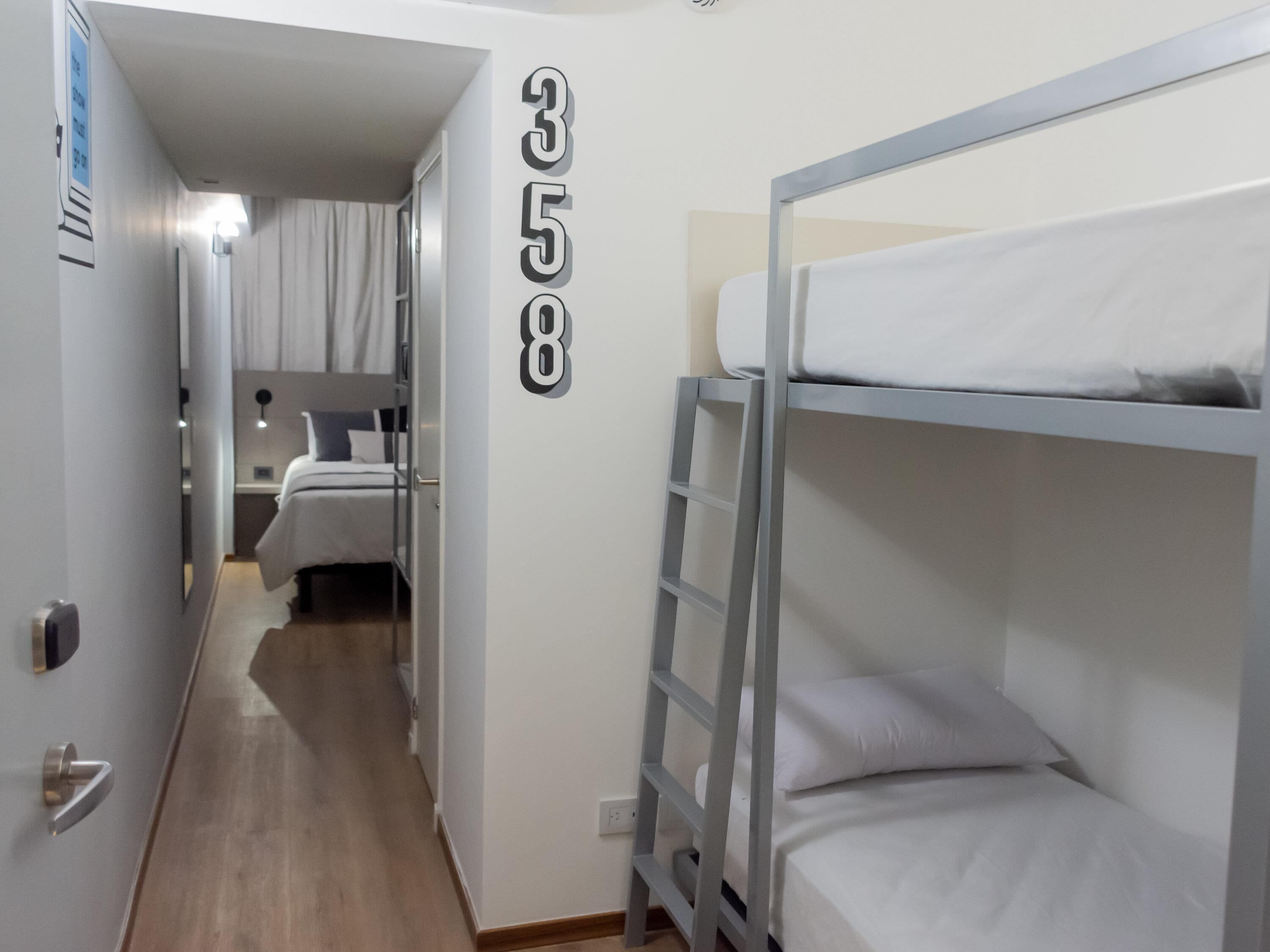A corridor with bunk beds, a door with a number, and a bed with a headboard.