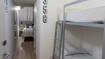 Een gang met stapelbedden, een deur met een nummer en een bed met hoofdeinde.