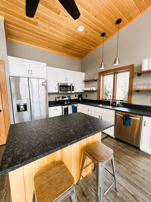 A modern kitchen with a central island, stainless steel appliances, wooden cabinets, and a window providing natural light.