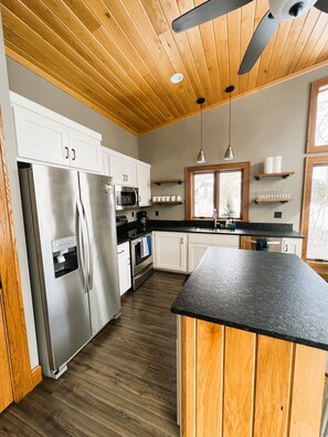 Eine moderne Küche mit Holzboden, Edelstahlgeräten und einer schwarzen Arbeitsplatte.