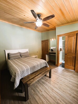 A bedroom with a bed, wooden flooring, a ceiling fan, and a wooden door.