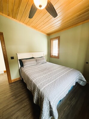 Ein Schlafzimmer mit Holzbalkendecke, einem Bett mit gemustertem Überwurf, einem Fenster und einer Tür.