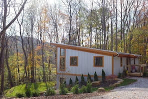 Una cabaña con fachada blanca y detalles de madera, rodeada de árboles y un sendero de grava.