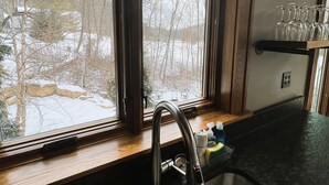 Une cuisine équipée d’un évier à deux bacs, d’un plan de travail en bois et d’une fenêtre donnant sur un paysage enneigé.