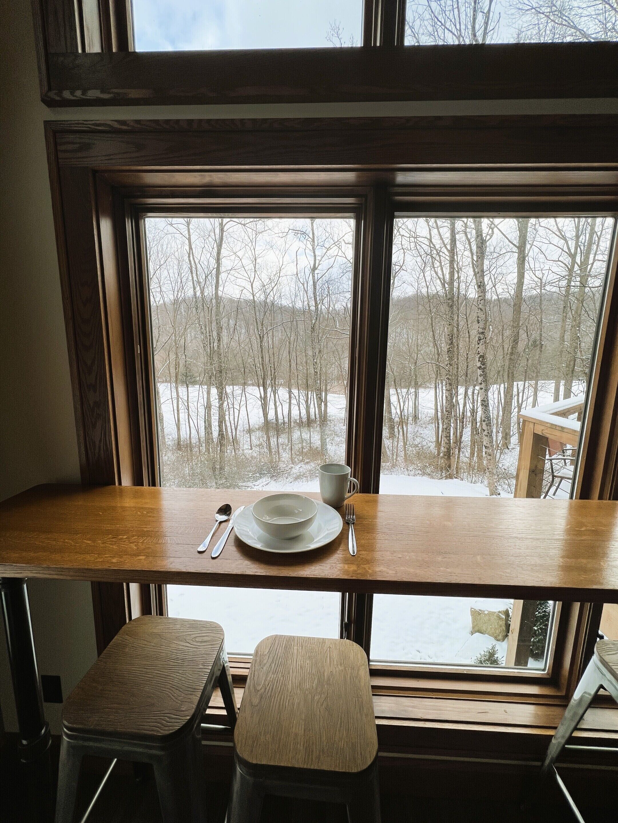 A dining area with a wooden table and bench, a window with a view of a snowy landscape.