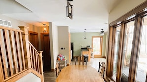Un vaste espace dédié à la salle à manger, avec une table et des chaises en bois, un escalier doté d’une rampe en bois, et de grandes fenêtres sur un des murs.