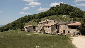 Un bâtiment en pierre comprenant plusieurs pièces et une cour, entouré d’une zone herbeuse et d’arbres.