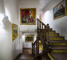 A staircase with wooden balusters and a handrail, flanked by three framed paintings on the walls.
