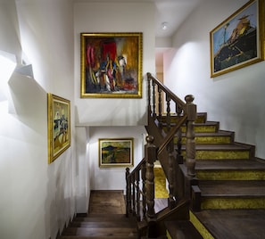 A staircase with wooden balusters and a handrail, flanked by three framed paintings on the walls.