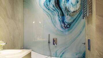 A modern bathroom with a marble wall, a freestanding bathtub, a toilet, and a vanity with a towel rack.
