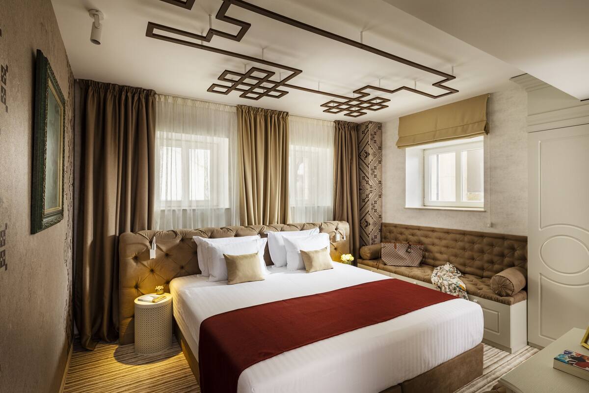 Quarto de hotel com uma cama grande, um sofá, uma mesa pequena e uma janela com cortinas.