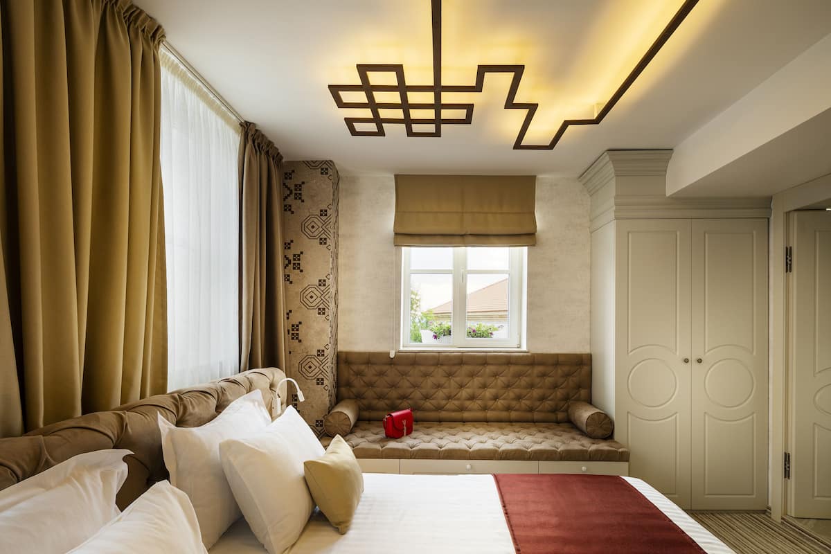 Um quarto com cama, janela com cortinas, um banco embutido e um armário.