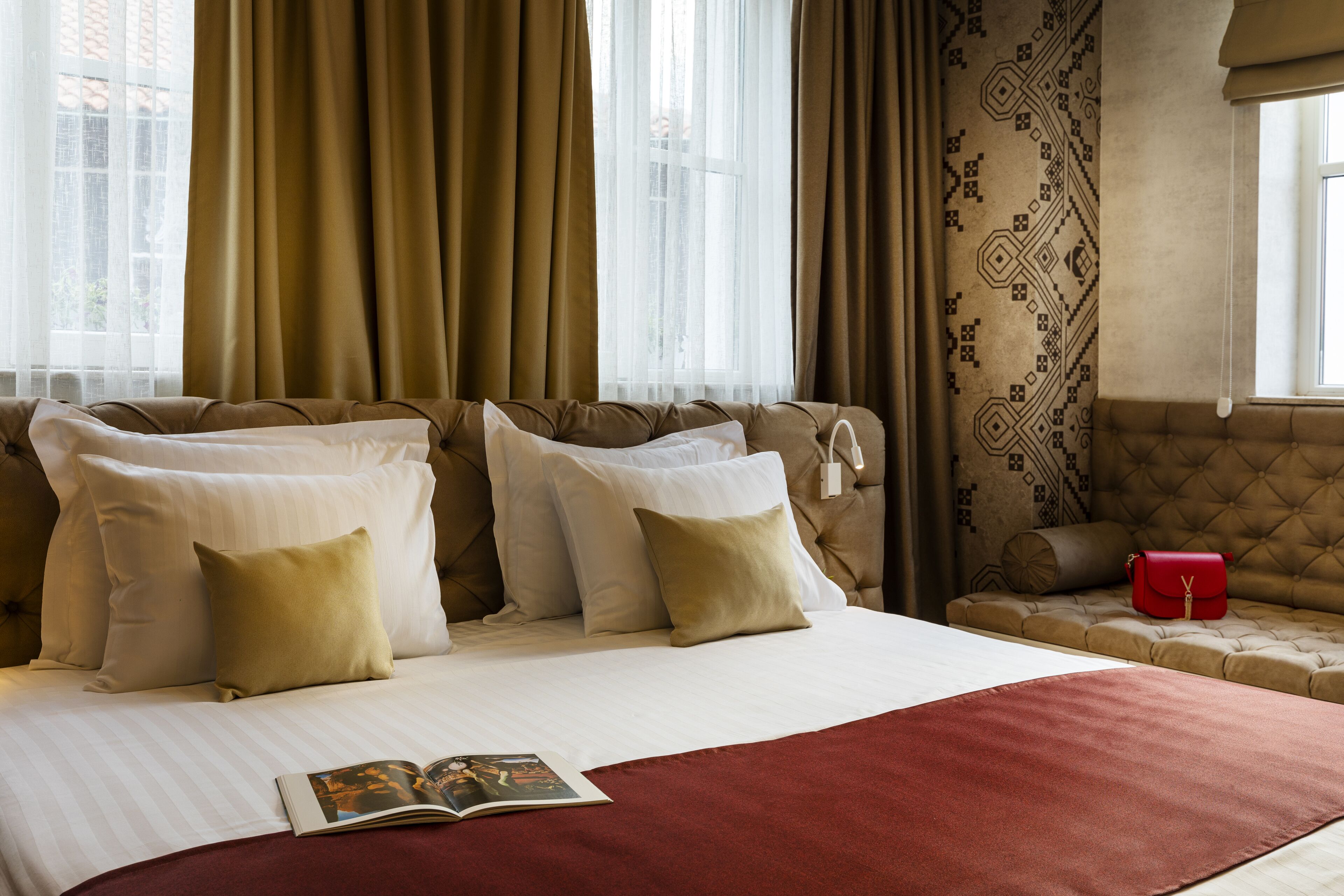 A hotel room with a large bed, a red throw blanket, and a red handbag on a bench.