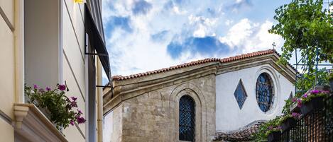 A courtyard with outdoor seating, stone walls, and a building with arched windows.