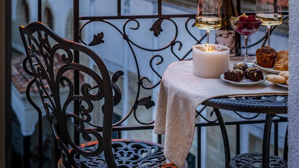 A balcony with a table set for a meal, a candle, and a bottle of wine, overlooking a sunset and a dome structure. - Gallery 37 (Plovdiv)