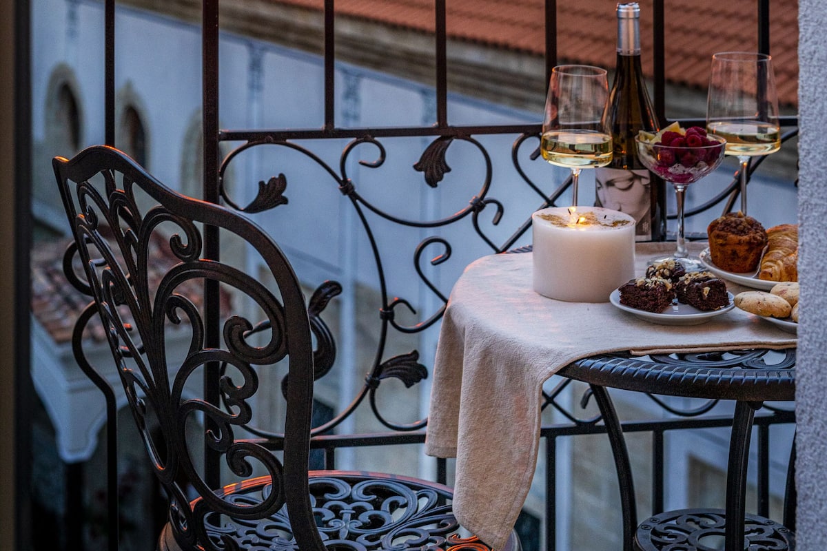 Varanda com mesa posta para refeição, vela e garrafa de vinho, com vista para um pôr do sol e uma estrutura em forma de cúpula.