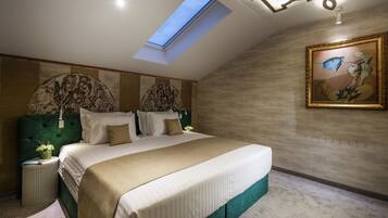 A bedroom with a skylight, a large bed, a painting, and a nightstand with a lamp.