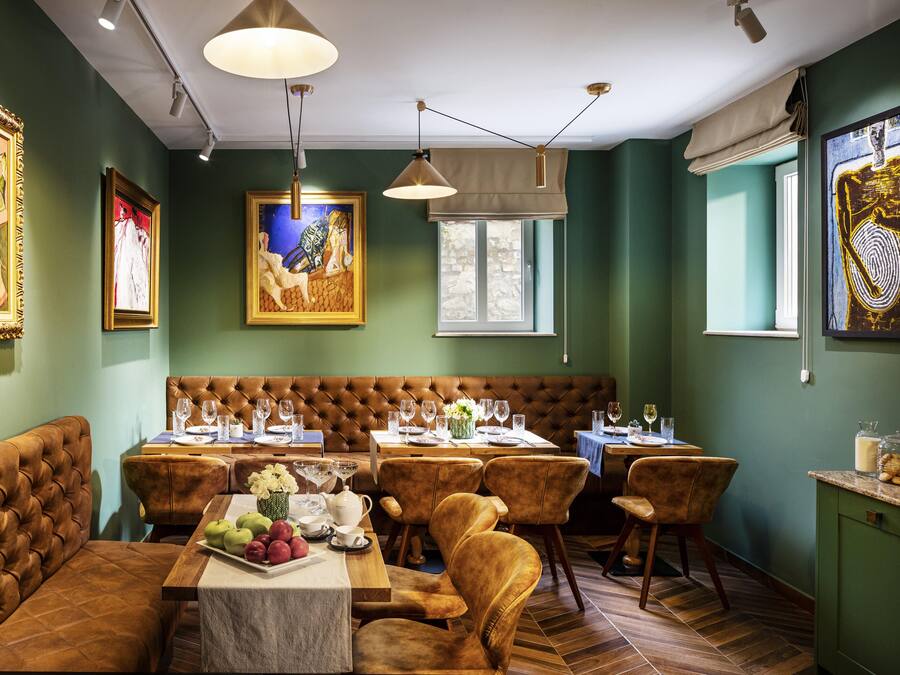 A restaurant with a green wall, wooden flooring, and a brown leather booth. Tables are set with wine glasses and plates.