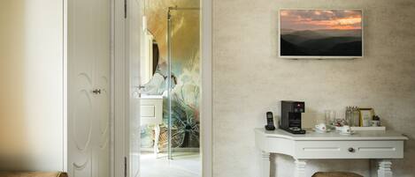 A hotel room with a desk, a chair, a sofa, and a painting of a sunset.