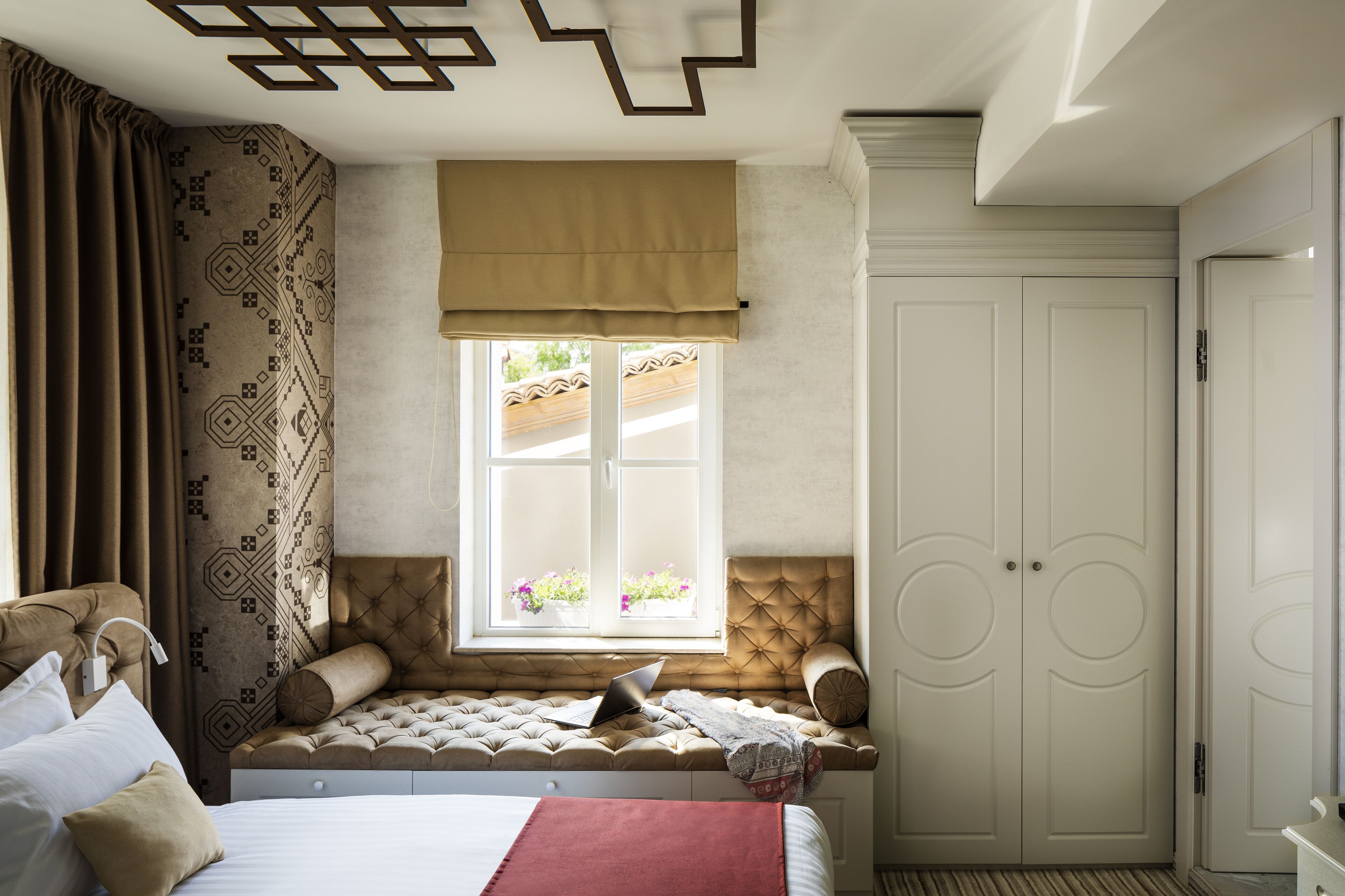 A bedroom with a bed, a window with a view of flowers, a wardrobe, and a bedside table.