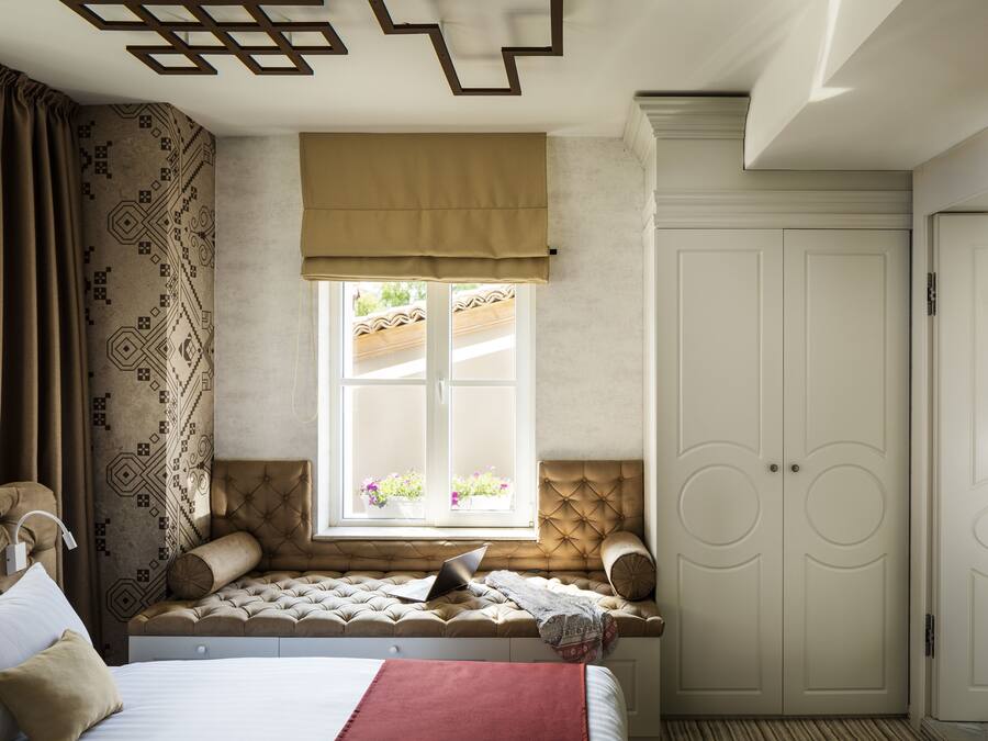 A bedroom with a bed, a window with a view of flowers, a wardrobe, and a bedside table.