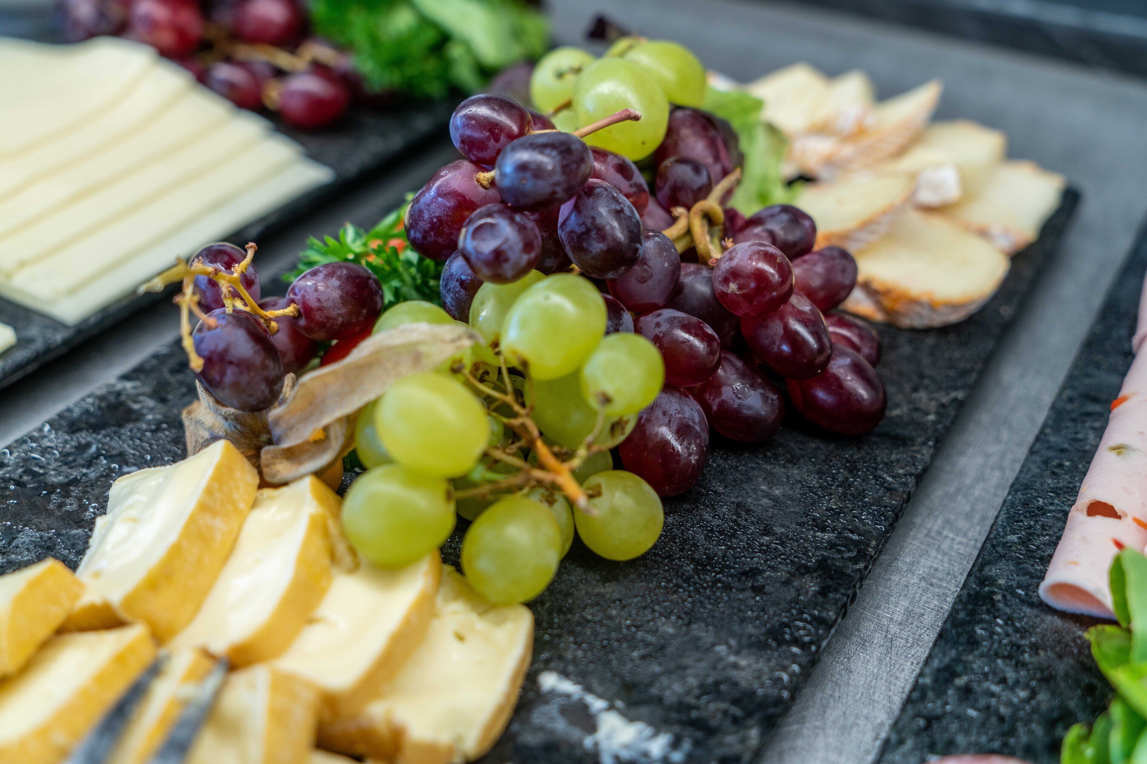 A charcuterie board with various cheeses, grapes, and sliced bread.