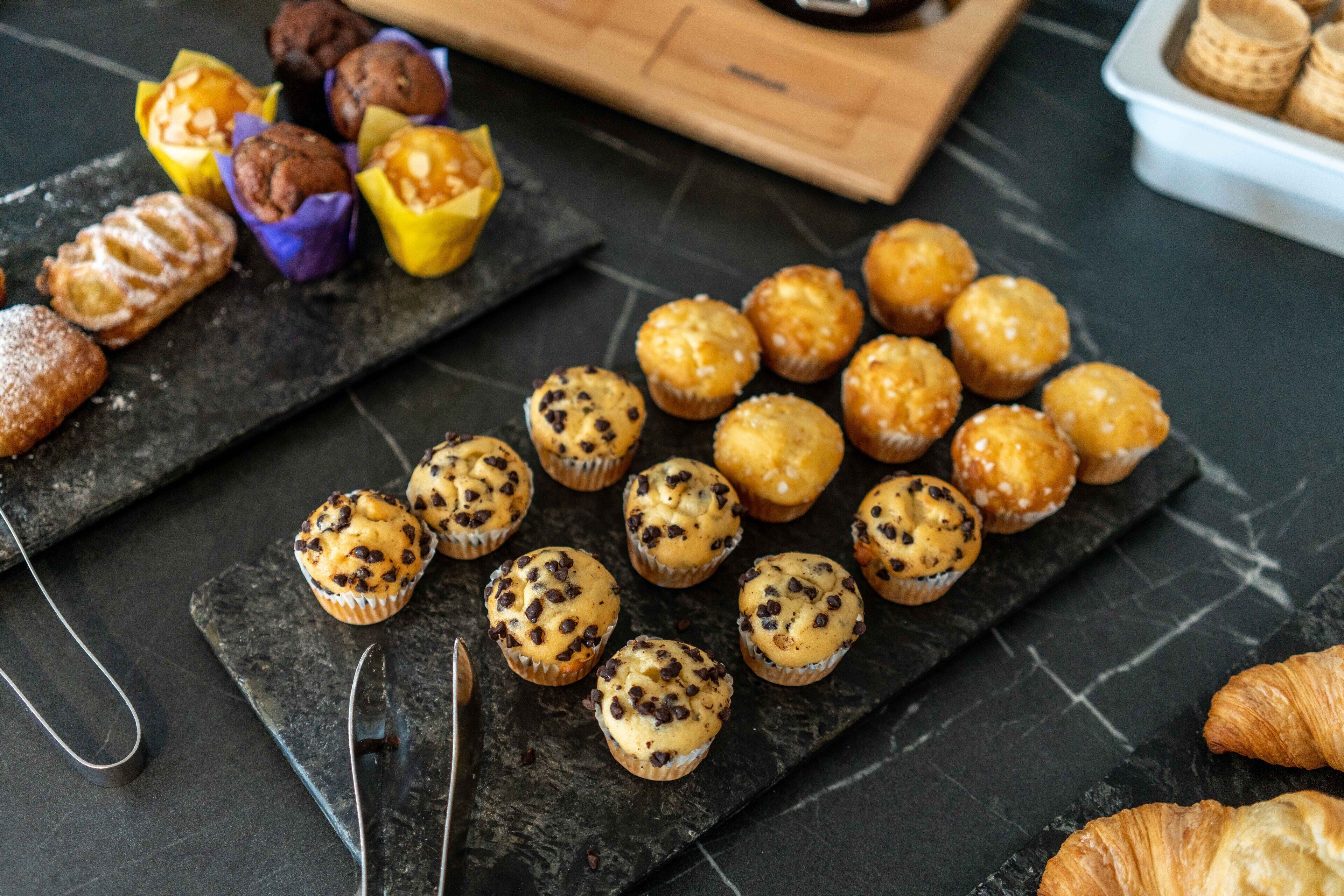 Diversas opciones de panadería sobre una tabla de piedra, incluyendo muffins y croissants.