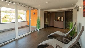 Ein modernes Hotelzimmer mit Balkon, einer Schiebeglastür, einer kleinen Küchenzeile und einer Sitzecke mit Stühlen.