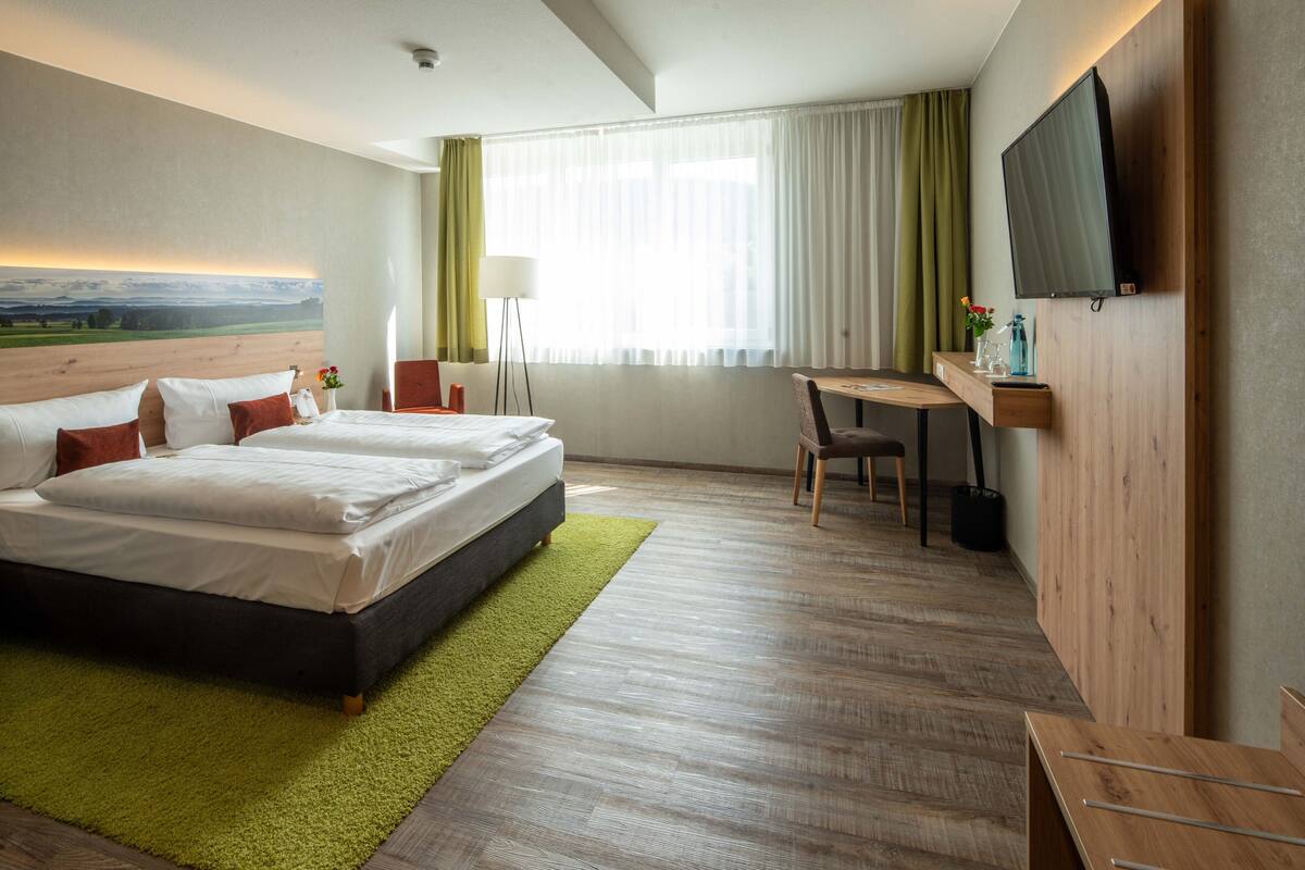Una habitación de hotel con una cama grande, un escritorio, una silla, un televisor y un cuadro en la pared.