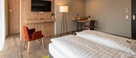 A hotel room with a bed, a desk, a chair, a TV, and a lamp.