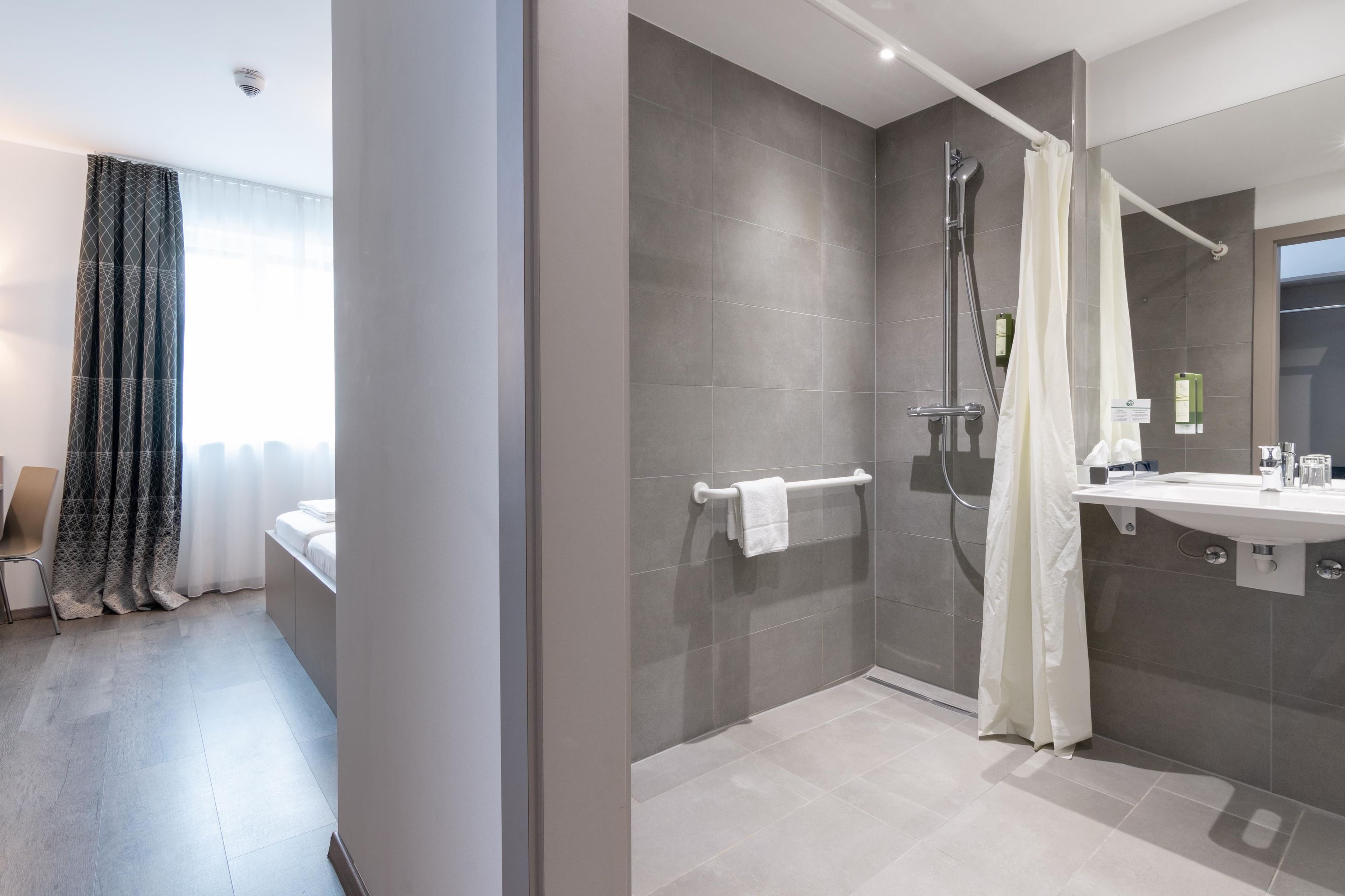 A modern bathroom with a walk-in shower, a glass-enclosed shower area, a white sink, and a large mirror.