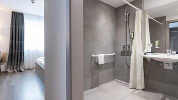 A modern bathroom with a walk-in shower, a glass-enclosed shower area, a white sink, and a large mirror.