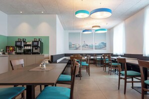 A restaurant with multiple tables and chairs, a coffee machine, and a mural on the wall.