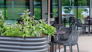 Outdoor seating with red umbrellas, a planter with greenery, and a building in the background.