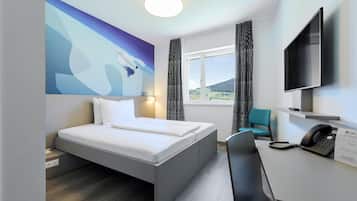 Habitación de hotel moderna con cama, escritorio, silla, televisor de pantalla plana y un cuadro en la pared.