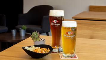 Dos vasos de cerveza sobre una mesa de madera con un cuenco de aperitivos y una pequeña planta en maceta.