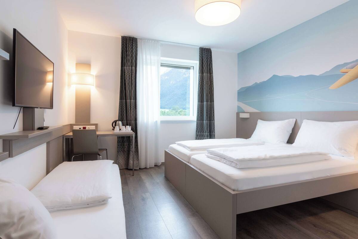 A hotel room with two beds, a desk, a chair, a TV, and a window with curtains.
