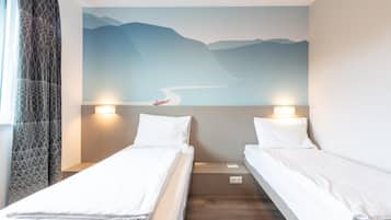 A hotel room with two single beds, a mural of a landscape on the wall, and a window with curtains.