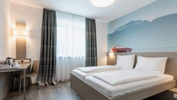 A hotel room with a bed, a desk, a chair, a coffee maker, and a wall with a mountain painting.