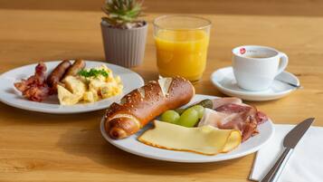 Een ontbijttafel met borden eten, een glas sinaasappelsap, een kop koffie en een kleine potplant.