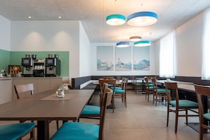 A modern dining area with multiple tables and chairs, a coffee machine, and a large window with a cityscape view. - Best Western Hotel Kiefersfelden (Kiefersfelden)