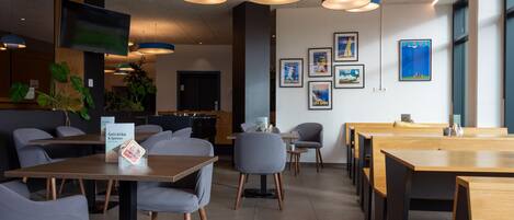 A modern cafe with wooden tables and chairs, pendant lighting, and framed artwork on the walls.