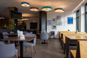 A modern cafe with wooden tables and chairs, pendant lighting, and framed artwork on the walls. - Best Western Hotel Kiefersfelden (Kiefersfelden)