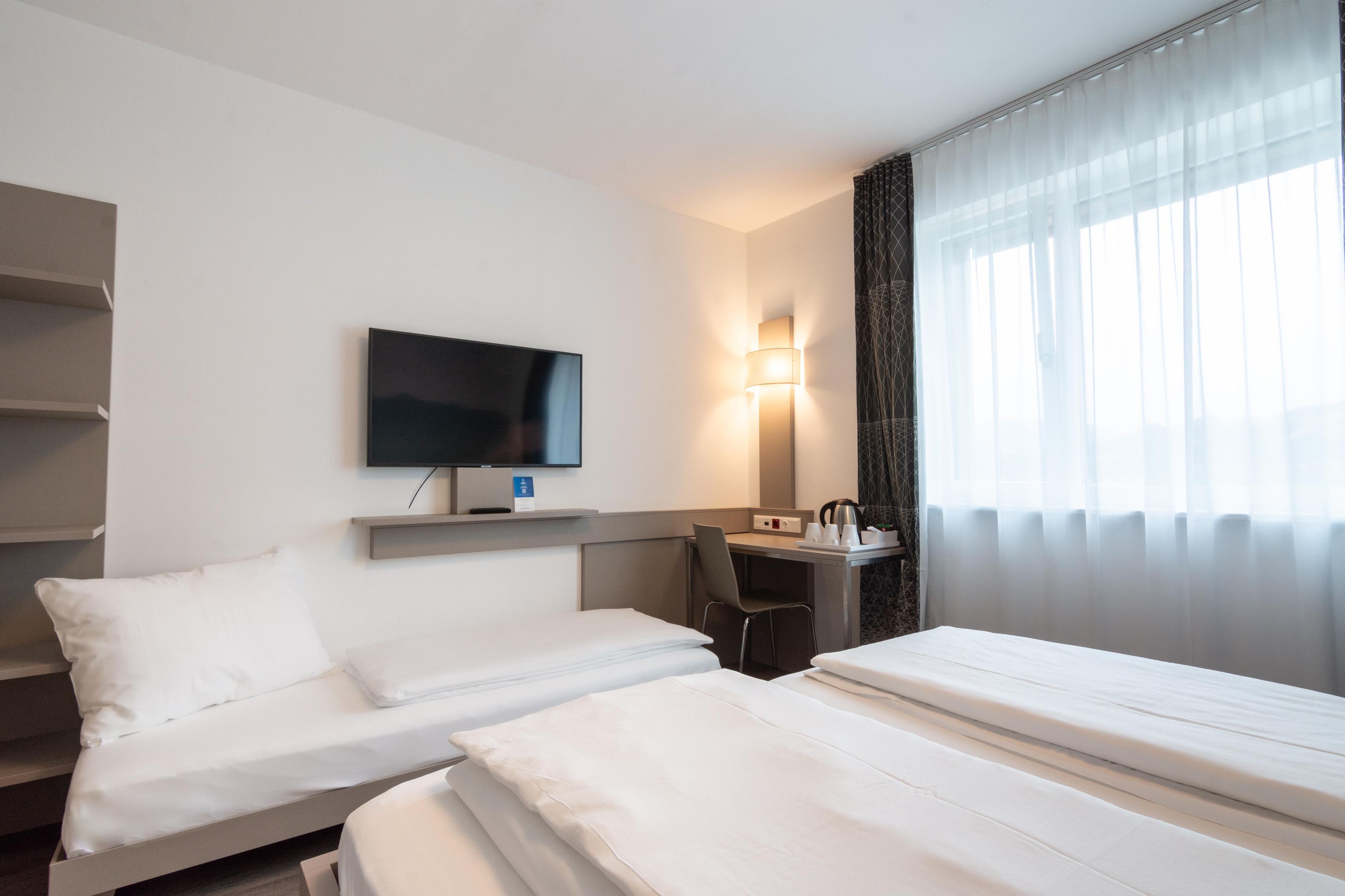 A hotel room with two beds, a desk, a television, and a window with curtains.