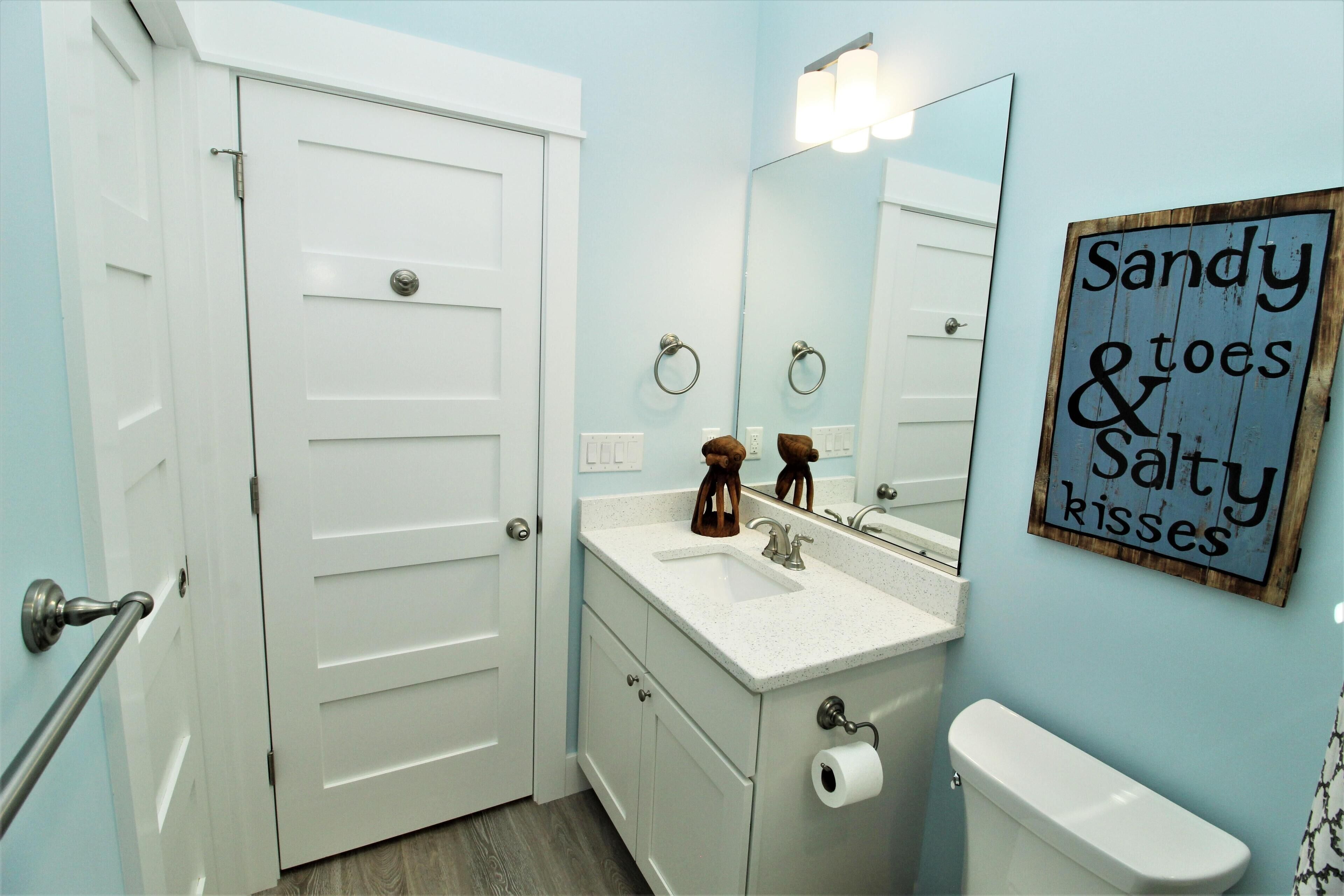 A bathroom with a white door, a sink with a mirror, and a sign on the wall.