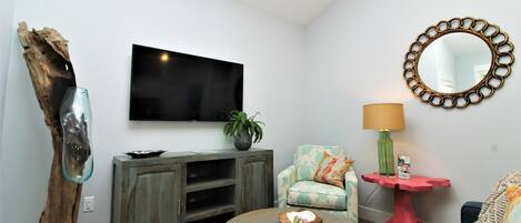 A living room with a flat-screen TV, a wooden cabinet, a round coffee table, a sofa, a red side table, and a mirror on the wall.