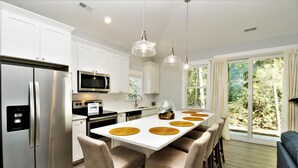A modern kitchen with white cabinets, stainless steel appliances, and a central island with chairs. - Beacon Quarters by KEES Vacations (Corolla)