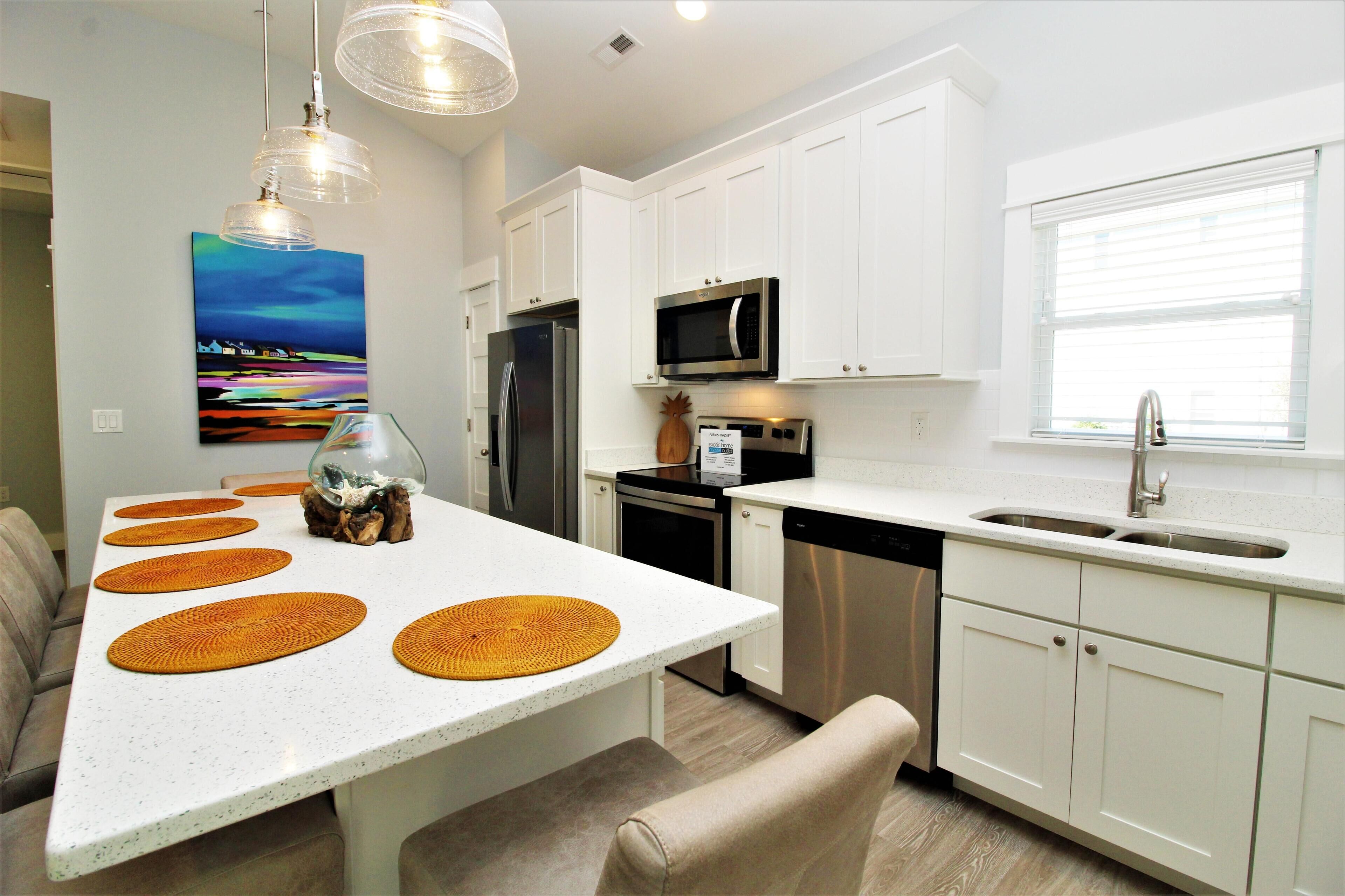 Une cuisine moderne avec des meubles blancs, des appareils en acier inoxydable et un coin repas comprenant une table blanche et des sets de table orange.