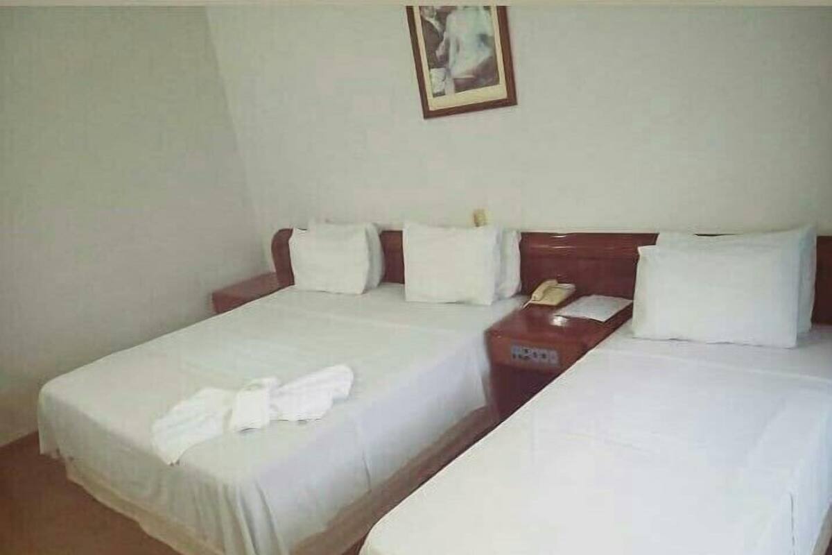 A hotel room with two beds, white linens, a wooden headboard, a bedside table with a telephone, and a framed picture on the wall.